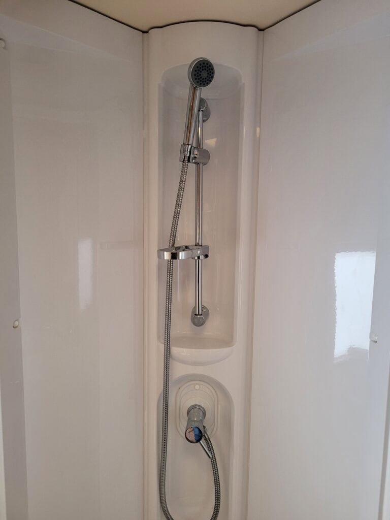 Shower unit with adjustable handheld showerhead and control knob in a compact caravan bathroom.