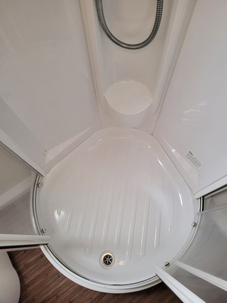 Shower cabin interior with white acrylic walls and a curved base, featuring a handheld showerhead an.