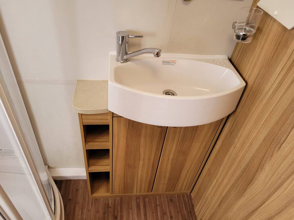 Bathroom sink with wooden cabinet and storage shelves.