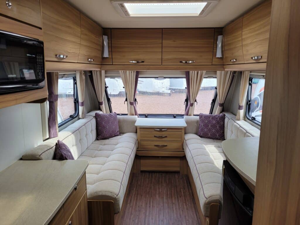 Caravan lounge interior featuring plush cushioned seating, storage cabinets, and large windows with.
