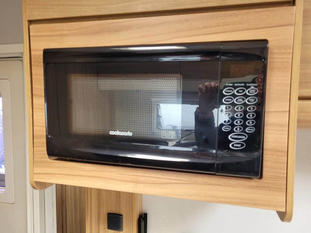 Modern black microwave oven installed in a wooden kitchen cabinet.