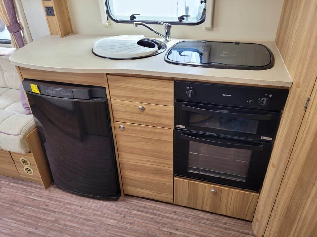 Compact caravan kitchen with sink, oven, and fridge.
