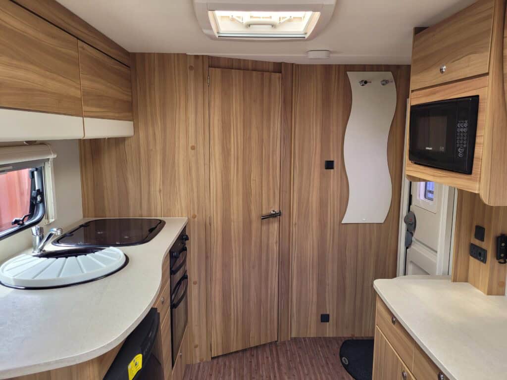 Cozy campervan kitchen with wooden cabinets, microwave, and compact appliances.