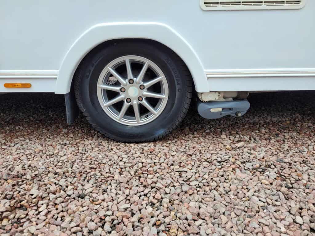 Close-up of a caravan wheel and wheel arch on gravel surface.