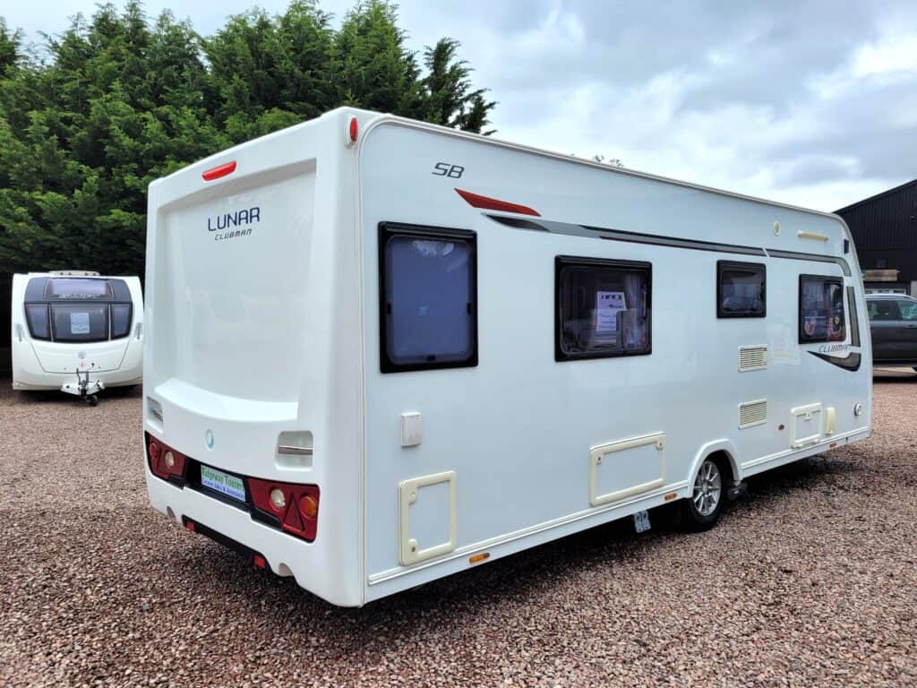 A modern white Lunar caravan parked outdoors on a gravel surface with trees in the background.