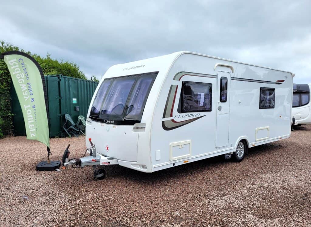 Modern white caravan with large windows parked outdoors on gravel surface.
