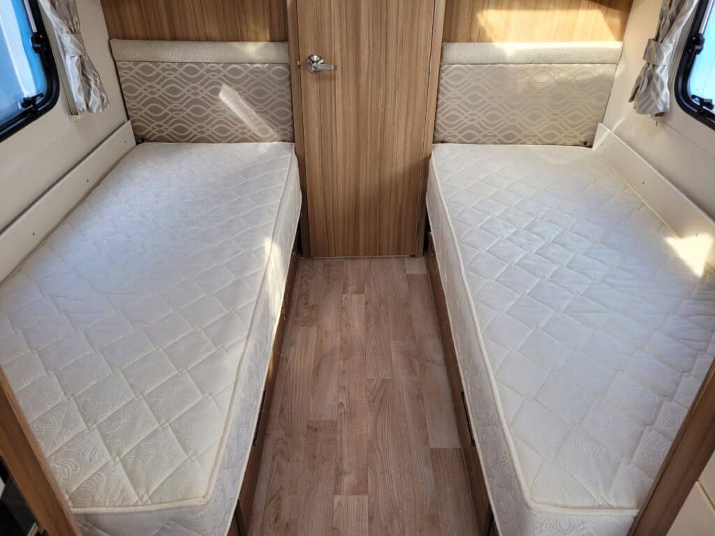 Interior of a Ridgeway Tourers caravan showing two single beds with mattresses, wooden flooring, and.
