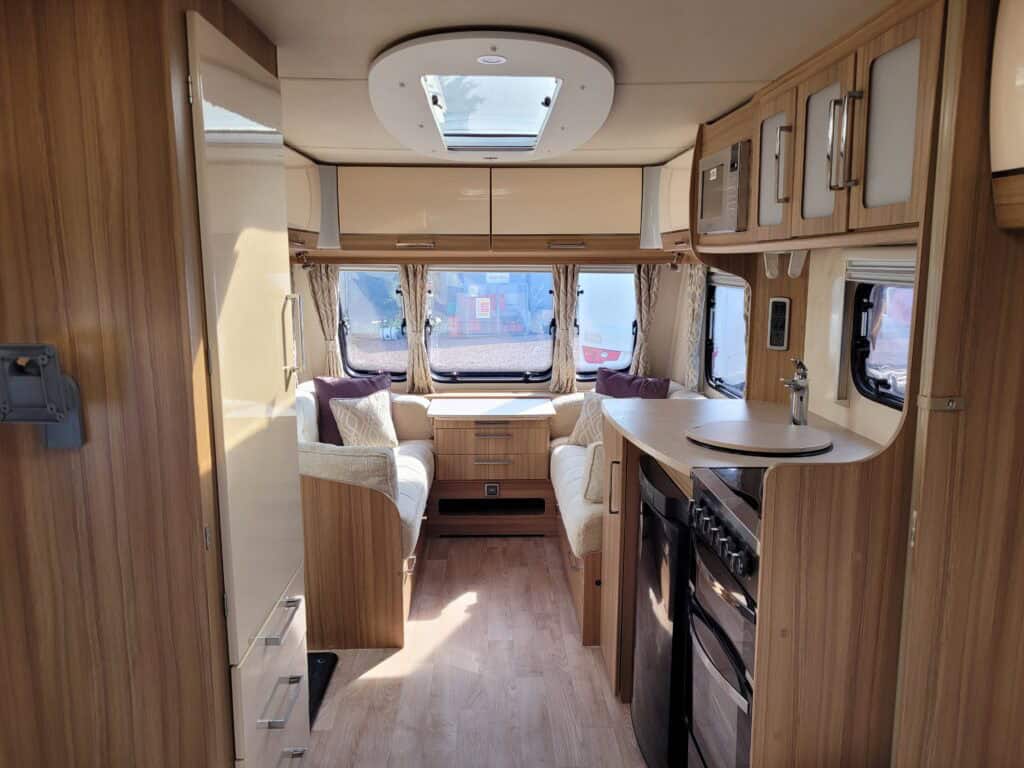 Interior view of a modern caravan with seating, kitchen, and large windows for a comfortable holiday.