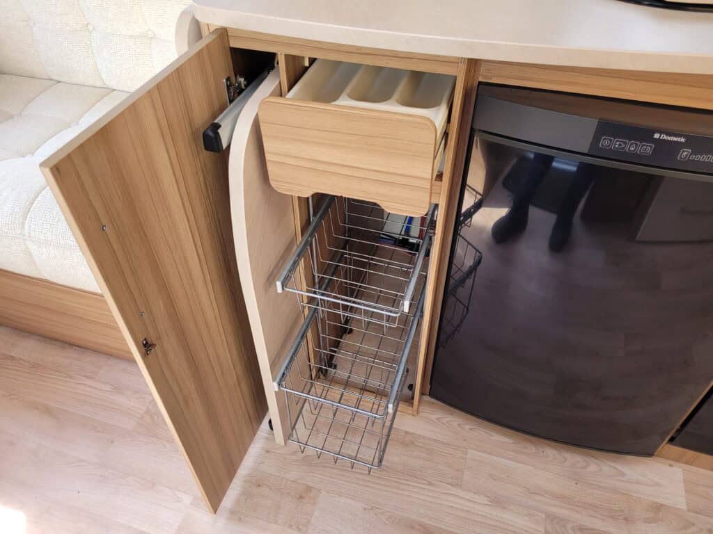 Efficient kitchen organisation with pull-out wire baskets and a wooden drawer in contemporary cabine.