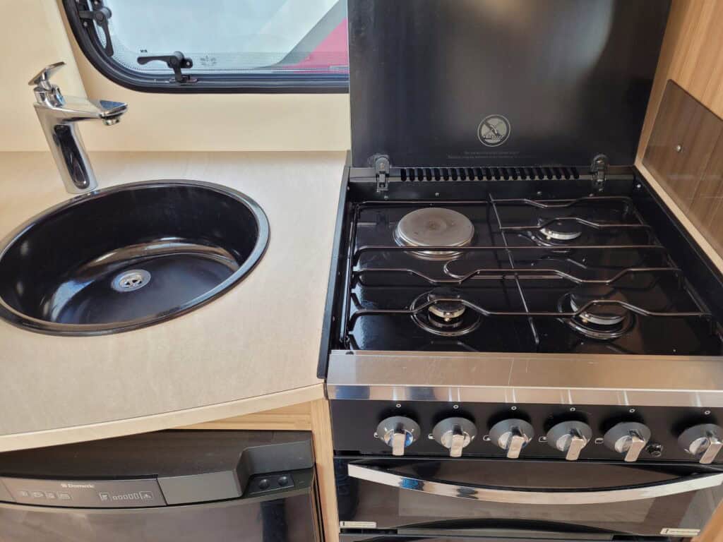Portable campervan kitchen with stove, sink, and storage for outdoor touring comfort.