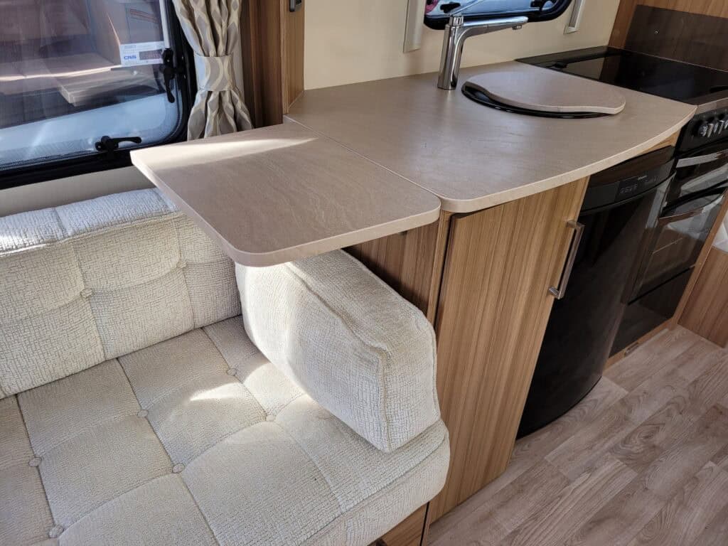 Interior view of a campervan kitchen with a beige cushioned seating area and wooden cabinetry, showc.