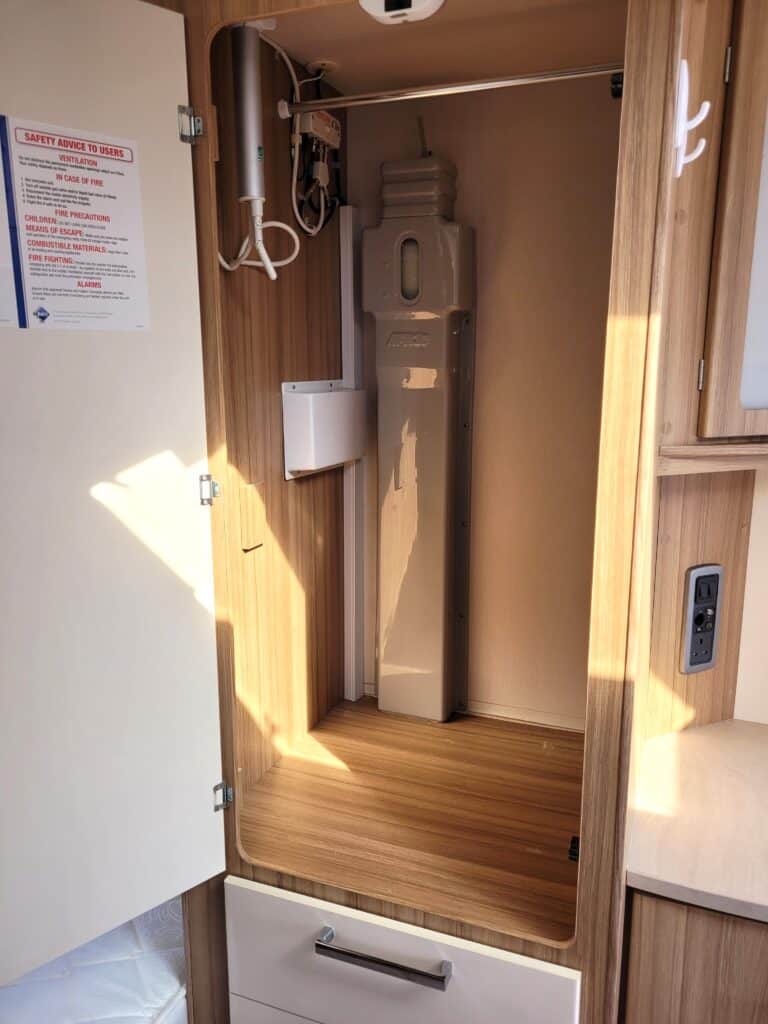 Compact camper van water heater installation in wooden cabinet.