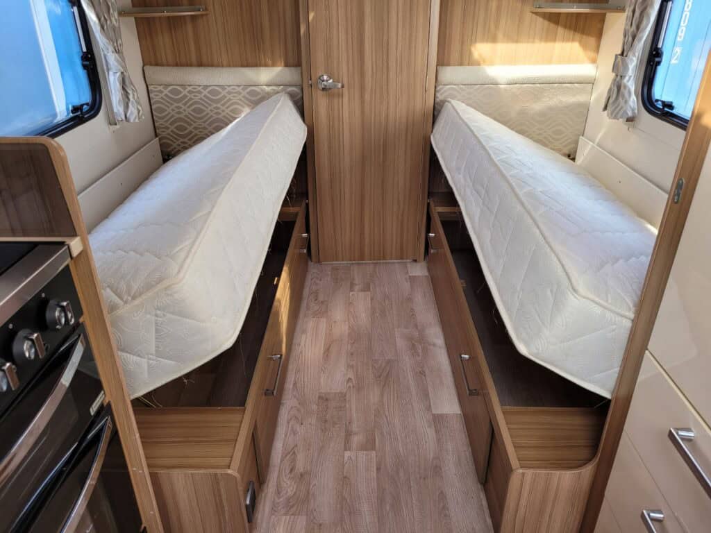 Interior of a campervan with twin beds, wooden cabinetry, and cozy design.