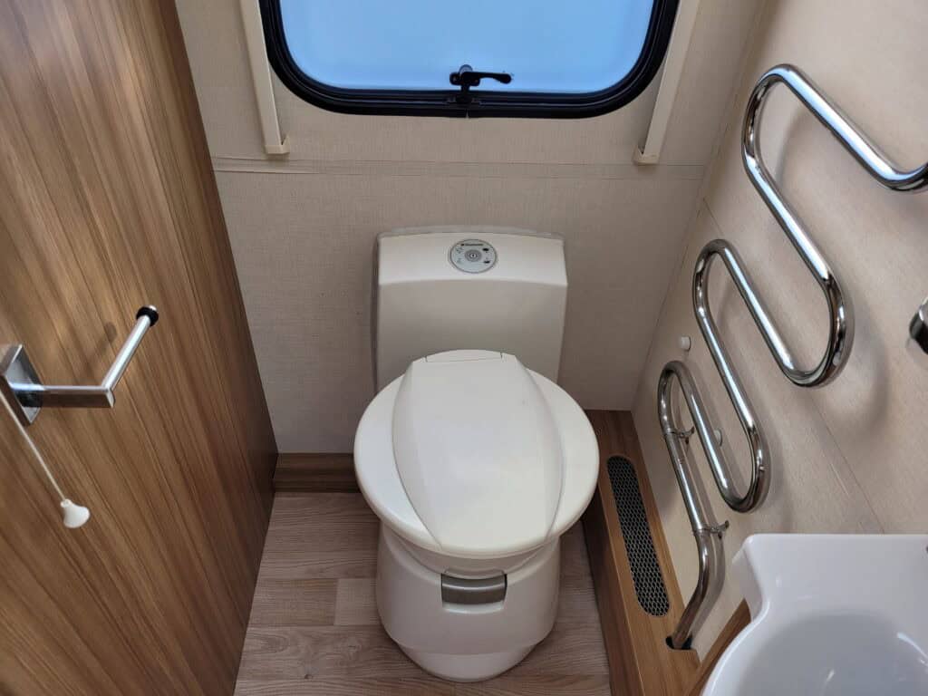 Compact toilet with heated towel rails and window in a campervan.