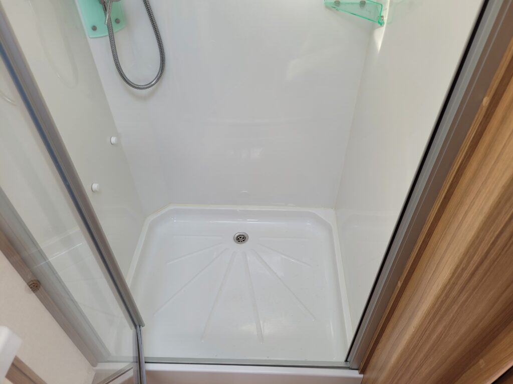 Compact shower cabin with modern design and white interior, featuring a handheld showerhead and glas.