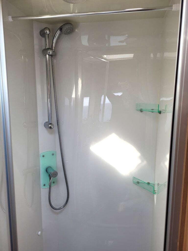 Accessible shower unit with adjustable handheld showerhead and sleek glass shelves for toiletries.