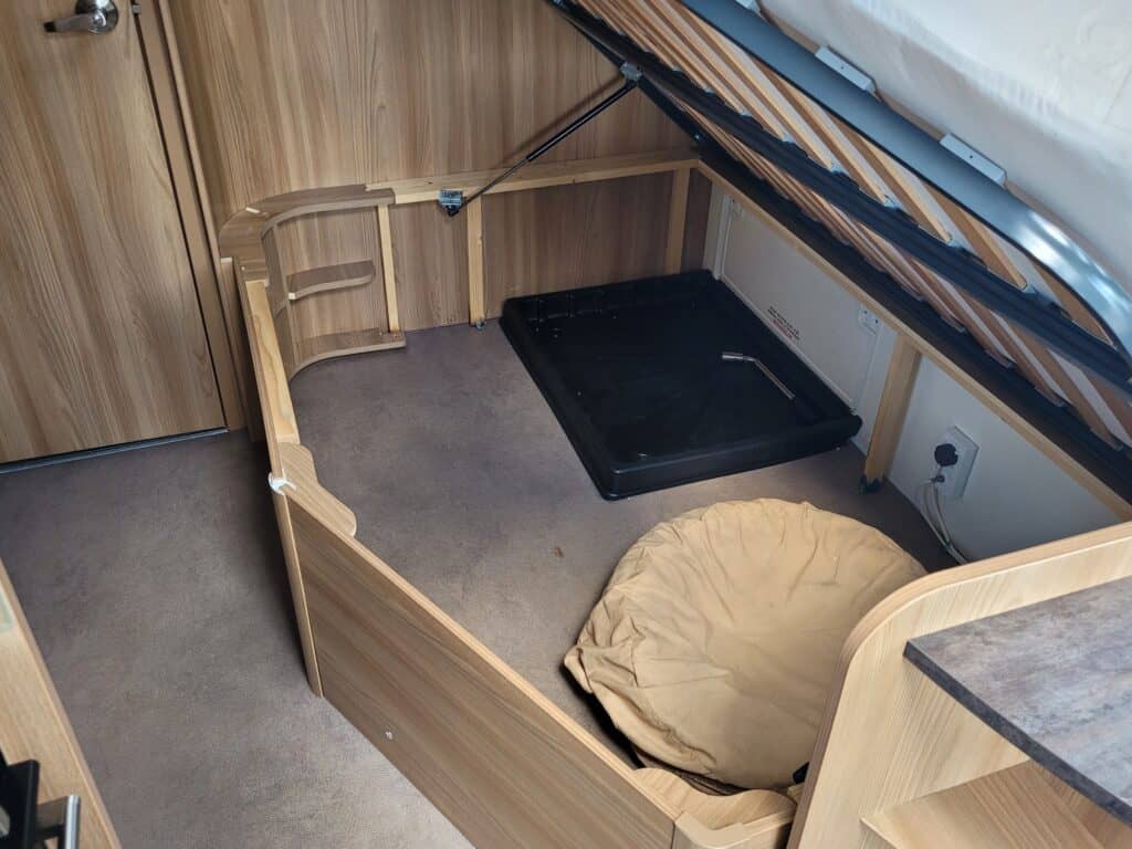 Compact camper van interior with a cozy bed and wooden furnishings.