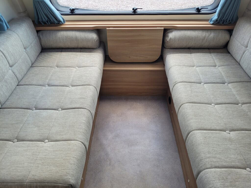 Spacious caravan seating area with light fabric cushions and wooden accents.