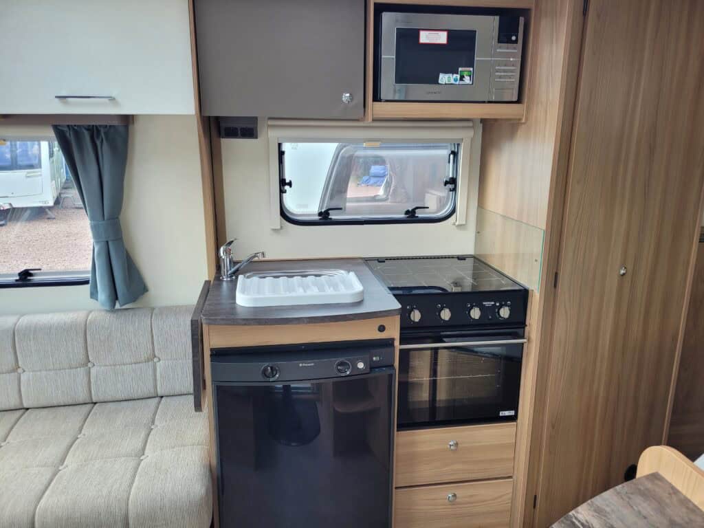 Kitchen in a caravan with oven, microwave, and window view.