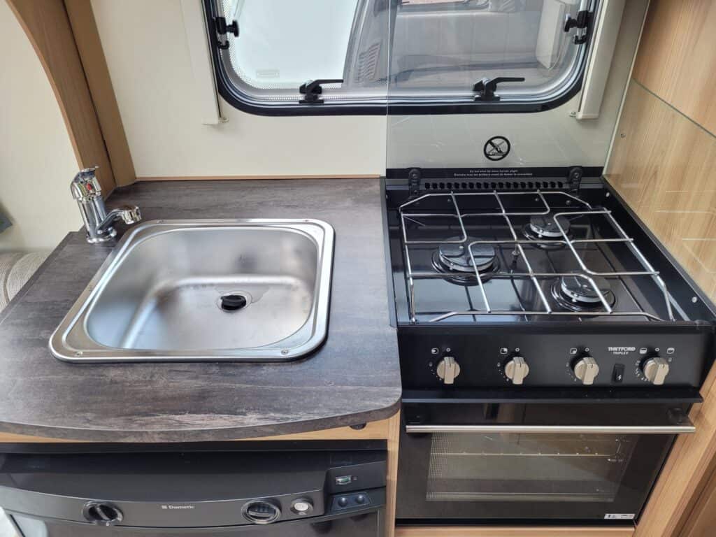 Compact campervan kitchen with sink and gas stove.