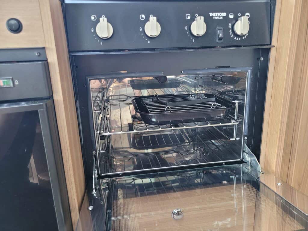 Oven with open door in a campervan kitchen setup, showcasing built-in appliances for mobile travel.
