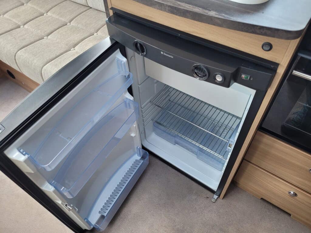 Small camper fridge with open door, revealing interior shelves and cooling system.