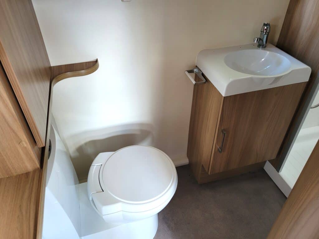 Small RV bathroom featuring a modern toilet and a compact sink with wooden storage cabinet.