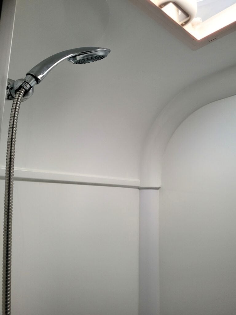 Shower head in a bright, minimalist bathroom with white walls and curved ceiling.